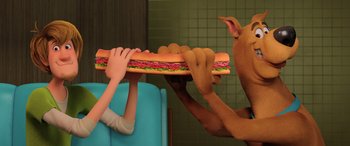 Movie still from “Scoob!” (2020), directed by Tony Cervone – A person holding onto a giant sandwich while another person holds onto a large sandwich; Medium shot, Over the shoulder angle