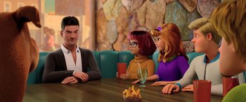 Movie still from “Scoob!” (2020), directed by Tony Cervone – A man sitting at a table next to two women; Medium shot, Over the shoulder angle