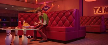 Movie still from “Scoob!” (2020), directed by Tony Cervone – A man sitting on a red couch in a restaurant; Wide shot, High angle