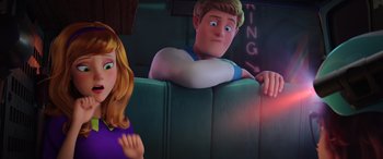 Movie still from “Scoob!” (2020), directed by Tony Cervone – A girl and a boy sitting on a couch in a room; Medium shot, Over the shoulder angle