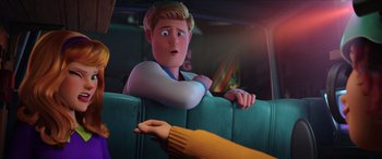 Movie still from “Scoob!” (2020), directed by Tony Cervone – A man sitting in the back of a car next to another man; Medium shot, Over the shoulder angle