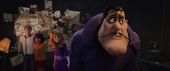 Movie still from “Scoob!” (2020), directed by Tony Cervone – A woman standing next to a man in a purple suit; Medium shot, Over the shoulder angle