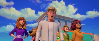 Movie still from “Scoob!” (2020), directed by Tony Cervone – A man standing next to a woman and a dog in front of a building; Medium shot, Low angle