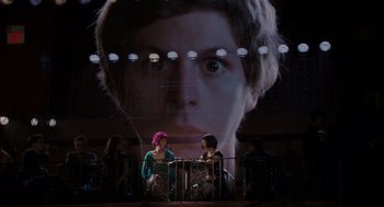 Movie still from “Scott Pilgrim vs. the World” (2010), directed by Edgar Wright – Two women are sitting in front of a large picture of a man's face; Extreme Wide shot, Over the shoulder angle