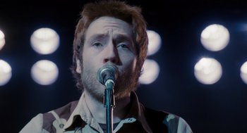 Movie still from “Scott Pilgrim vs. the World” (2010), directed by Edgar Wright – A man with a beard is singing into a microphone; Close Up shot, Over the shoulder angle