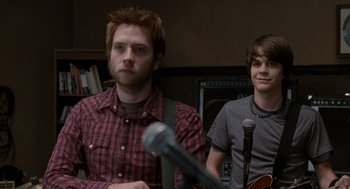 Movie still from “Scott Pilgrim vs. the World” (2010), directed by Edgar Wright – Two young men standing next to each other in front of microphones; Medium shot, Over the shoulder angle