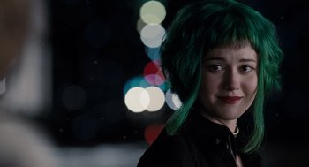 A woman with green hair standing in front of blurry lights