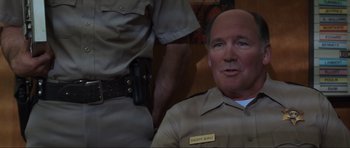 Movie still from “Scream” (1996), directed by Wes Craven – A man in a uniform sitting in front of another man in a uniform; Close Up shot, High angle