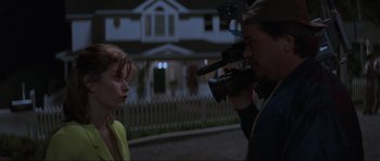 Movie still from “Scream” (1996), directed by Wes Craven – A man filming a woman in front of a white house; Medium shot, Over the shoulder angle