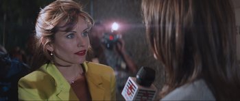 Movie still from “Scream” (1996), directed by Wes Craven – A woman in a yellow jacket is being interviewed by a camera; Close Up shot, Over the shoulder angle