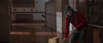 Movie still from “Scream” (1996), directed by Wes Craven – A man in a hat and a red and green shirt is sweeping the floor; Wide shot, Low angle