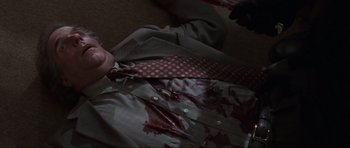 Movie still from “Scream” (1996), directed by Wes Craven – A man in a suit and tie laying on the floor; Medium shot, High angle