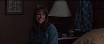 Movie still from “Scream” (1996), directed by Wes Craven – A young woman smiles for the camera in front of a lamp; Close Up shot, Over the shoulder angle