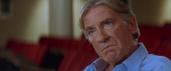 Movie still from “Scream 2” (1997), directed by Wes Craven – An older man sitting in front of a red couch; Close Up shot, Low angle