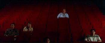 Movie still from “Scream 2” (1997), directed by Wes Craven – A man sitting in an empty theater with a woman taking a picture; Wide shot, High angle
