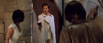 Movie still from “Scream 2” (1997), directed by Wes Craven – A man in a trench coat holding a gun in front of a mirror; Medium shot, Over the shoulder angle