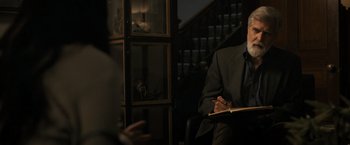 Movie still from “Scream VI” (2023), directed by Matt Bettinelli-Olpin – A man sitting in a chair writing on a piece of paper; Medium shot, Over the shoulder angle