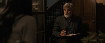 Movie still from “Scream VI” (2023), directed by Matt Bettinelli-Olpin – An older man sitting in front of a staircase writing in a notebook; Medium shot, Over the shoulder angle
