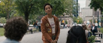 Movie still from “Scream VI” (2023), directed by Matt Bettinelli-Olpin – A person standing on a sidewalk near a park; Medium shot, Over the shoulder angle