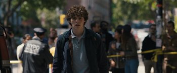 Movie still from “Scream VI” (2023), directed by Matt Bettinelli-Olpin – A young man walking down the street in a crowd of onlookers; Close Up shot, Over the shoulder angle