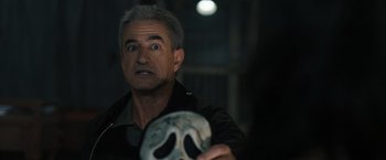 Movie still from “Scream VI” (2023), directed by Matt Bettinelli-Olpin – An older man holding up a mask in front of his face; Close Up shot, Over the shoulder angle