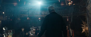 Movie still from “Scream VI” (2023), directed by Matt Bettinelli-Olpin – An older man standing in front of a group of people in a theater; Wide shot, Low angle