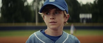 Movie still from “Secret Headquarters” (2022), directed by Henry Joost – A young boy wearing a baseball uniform and a hat; Close Up shot, Over the shoulder angle