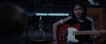 Movie still from “Secret Headquarters” (2022), directed by Henry Joost – A woman sitting in a chair holding a red guitar; Medium shot, High angle