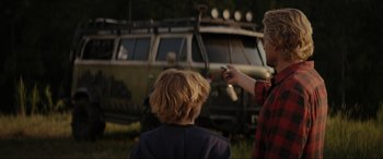 Movie still from “Secret Headquarters” (2022), directed by Henry Joost – Two children are standing in front of an army vehicle; Medium shot, Over the shoulder angle