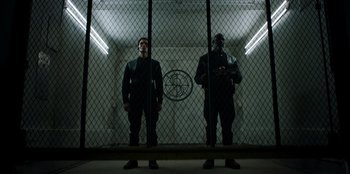Movie still from “Secret Society of Second Born Royals” (2020), directed by Anna Mastro – Two men standing next to each other in front of a fence; Wide shot, Low angle