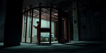 Movie still from “Secret Society of Second Born Royals” (2020), directed by Anna Mastro – A person standing in a cage in a room; Wide shot, High angle