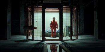 Movie still from “Secret Society of Second Born Royals” (2020), directed by Anna Mastro – A man in an orange suit standing in a room; Wide shot, Low angle