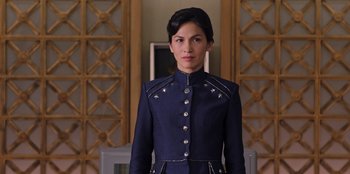 Movie still from “Secret Society of Second Born Royals” (2020), directed by Anna Mastro – A woman in a blue suit standing in front of a wall; Medium shot, Low angle