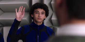 Movie still from “Secret Society of Second Born Royals” (2020), directed by Anna Mastro – A young man is holding his hand up in the air while wearing a blue and black jacket; Close Up shot, Overhead angle