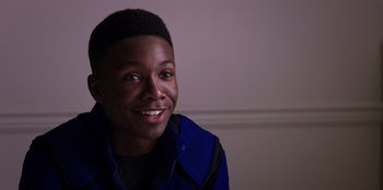 Movie still from “Secret Society of Second Born Royals” (2020), directed by Anna Mastro – A young man smiling for the camera in front of a white wall; Close Up shot, Over the shoulder angle