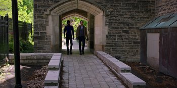 Movie still from “Secret Society of Second Born Royals” (2020), directed by Anna Mastro – Two men walking down a brick path under an archway; Wide shot, High angle