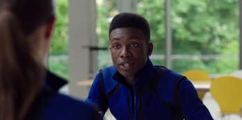 Movie still from “Secret Society of Second Born Royals” (2020), directed by Anna Mastro – A young man in a blue jacket is looking at the camera; Close Up shot, Over the shoulder angle