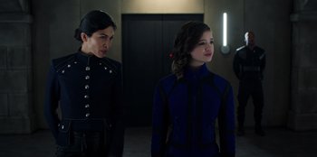 Movie still from “Secret Society of Second Born Royals” (2020), directed by Anna Mastro – Two women standing next to each other in front of an elevator; Medium shot, Over the shoulder angle