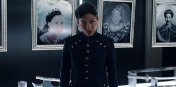 Movie still from “Secret Society of Second Born Royals” (2020), directed by Anna Mastro – A woman in a military uniform standing in front of three portraits; Close Up shot, Over the shoulder angle