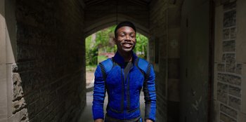 Movie still from “Secret Society of Second Born Royals” (2020), directed by Anna Mastro – A man in a blue and black jacket standing in a tunnel; Medium shot, Low angle