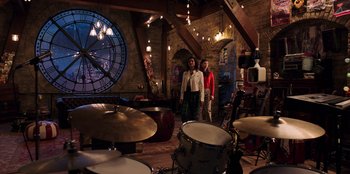 Movie still from “Secret Society of Second Born Royals” (2020), directed by Anna Mastro – Two people are standing in a room with a clock in the background; Wide shot, High angle