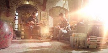 Movie still from “Secret Society of Second Born Royals” (2020), directed by Anna Mastro – Two men sitting in a living room with guitars; Wide shot, Low angle