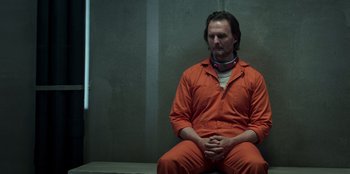 Movie still from “Secret Society of Second Born Royals” (2020), directed by Anna Mastro – A man in an orange jumpsuit sitting in a cell; Medium shot, High angle