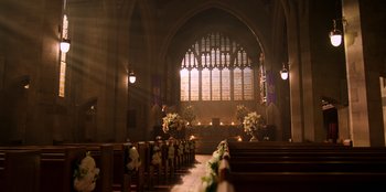 Movie still from “Secret Society of Second Born Royals” (2020), directed by Anna Mastro – A church filled with pews and flowers in front of a large window; Extreme Wide shot, High angle