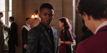 Movie still from “Secret Society of Second Born Royals” (2020), directed by Anna Mastro – A man in a suit and tie standing in front of a crowd; Close Up shot, Over the shoulder angle