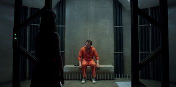 Movie still from “Secret Society of Second Born Royals” (2020), directed by Anna Mastro – A man in an orange jumpsuit sitting on a bench; Wide shot, High angle