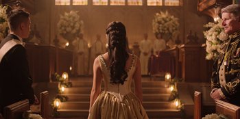 Movie still from “Secret Society of Second Born Royals” (2020), directed by Anna Mastro – A woman standing in front of a group of people in a church; Medium shot, Over the shoulder angle