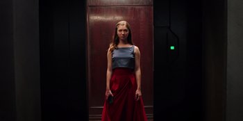 Movie still from “Secret Society of Second Born Royals” (2020), directed by Anna Mastro – A woman standing in front of an elevator holding a cell phone; Medium shot, Low angle