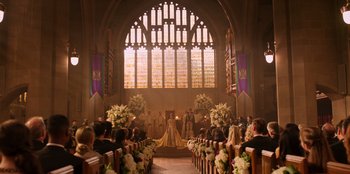 Movie still from “Secret Society of Second Born Royals” (2020), directed by Anna Mastro – A wedding ceremony in an old church with flowers in front; Extreme Wide shot, High angle