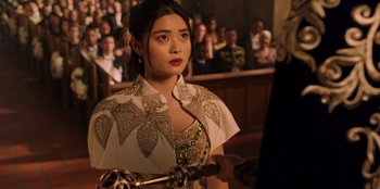 Movie still from “Secret Society of Second Born Royals” (2020), directed by Anna Mastro – A beautiful young lady wearing a white dress and holding an umbrella in front of an audience; Close Up shot, Over the shoulder angle